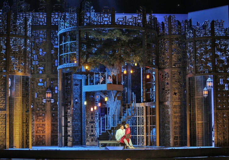 Young lovers sit together in the garden of a beautiful estate, in a theatre production. 