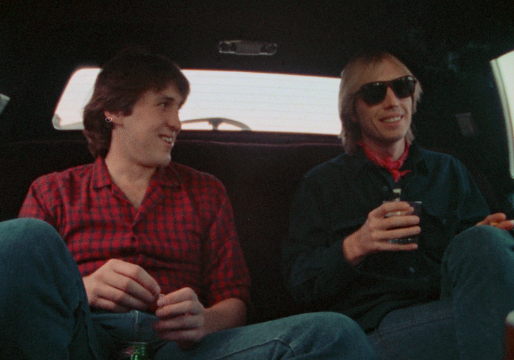 Two men sit in the back of a cab, chatting.