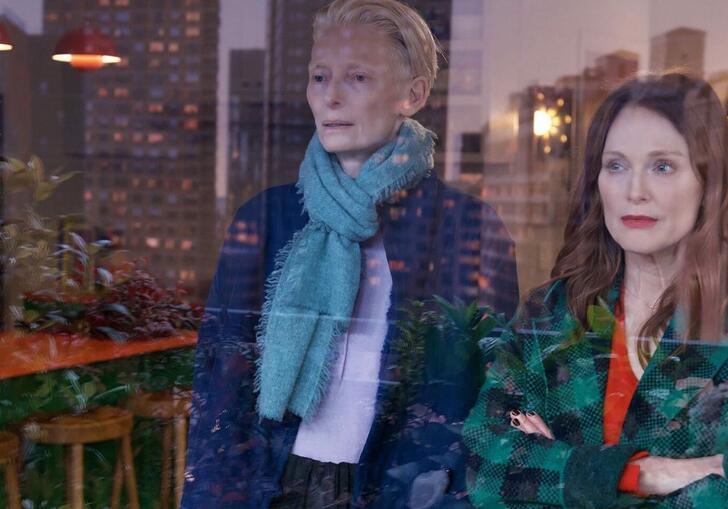 Two middle aged women stare out a window over a cityscape.