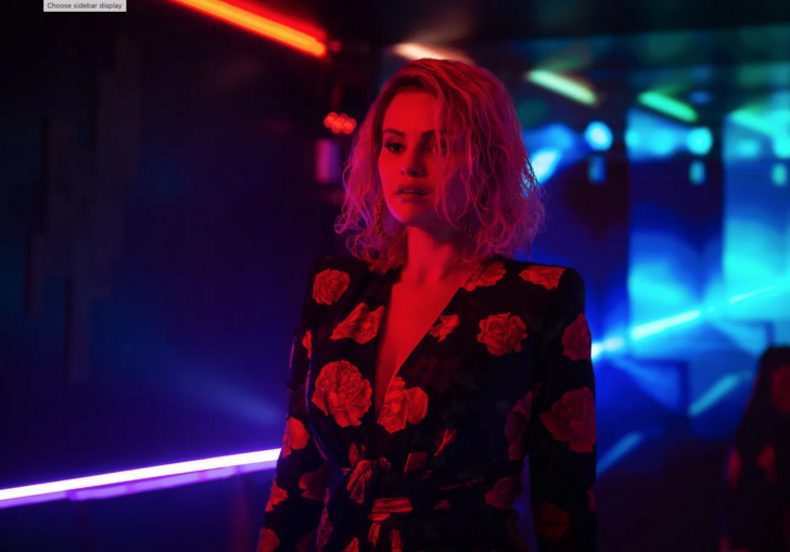 A woman stands in a blue, dark corridor, bathed in red light.