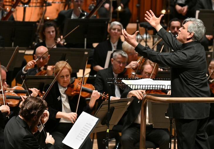 Sir Antonio Pappano conducting the London Symphony Orchestra, facing the Orchestra on the conductor's podium, with both hands raised in the air