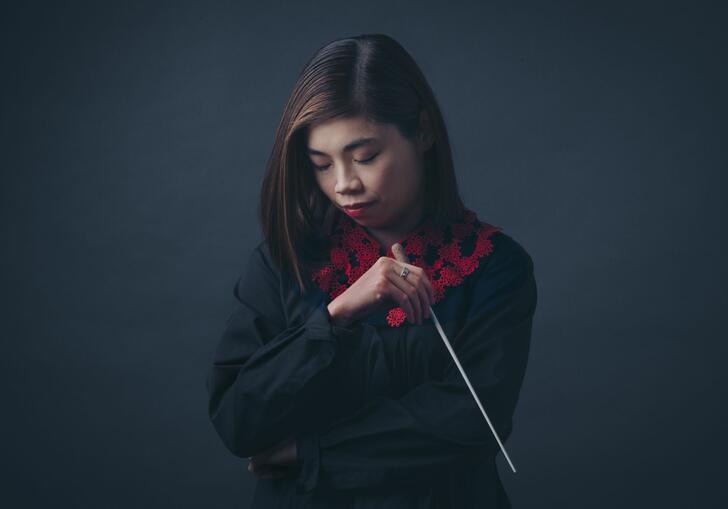 Conductor Elim Chan holding her baton and looking down.