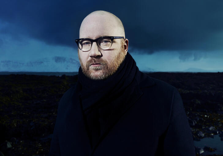Portrait of Jóhann Jóhannsson against a blue and black background