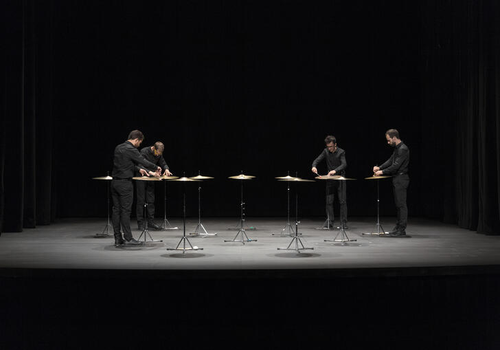 4 percussionists standing around an installation of 12 suspended cymbals