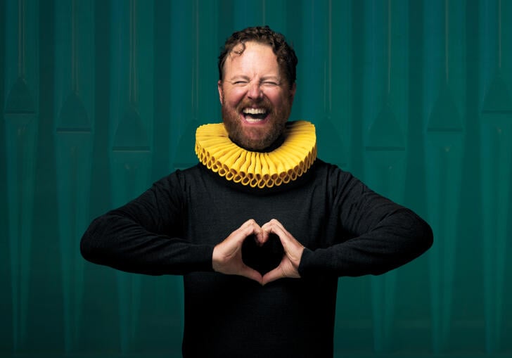 A person with a yellow collar around their neck makes a love heart symbol with their hands.