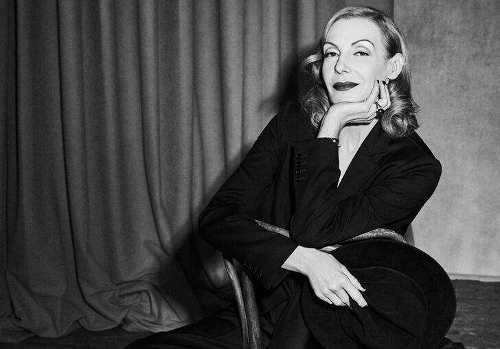 Black and white image of Ute Lemper sat backwards on a chair with her hand on her chin