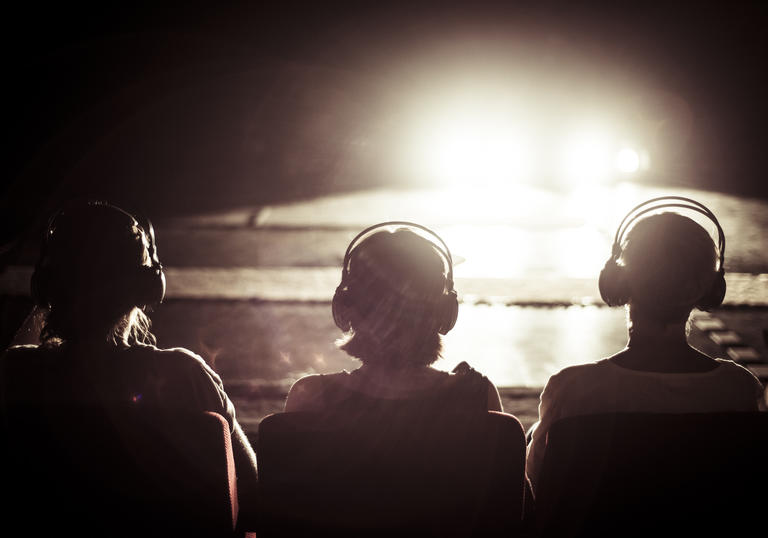 Image of three people with headphones looking into a bright light 