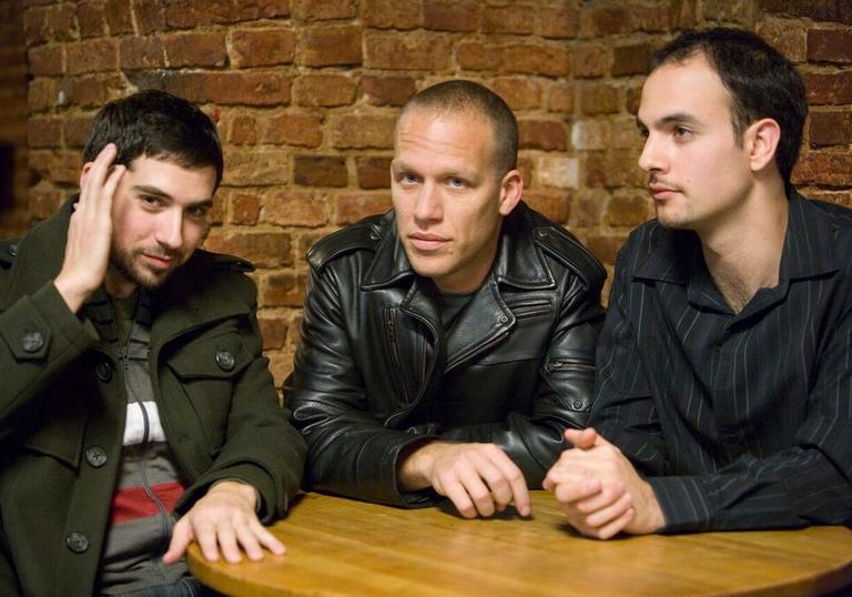 The Avishai Cohen trio wearing dark jackets sitting at a wooden table