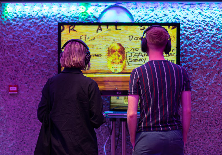 A couple with headphones on looking at a screen