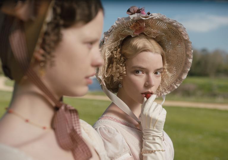 A young woman wearing a bonnet looks off-screen and seductively holds a piece of food up to her mouth.