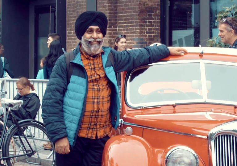 man wearing a turban puts his arm over a red car