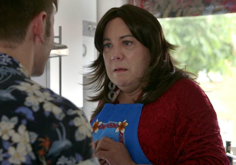 Women is standing with apron on in her kitchen talking to a man with his back to the camera