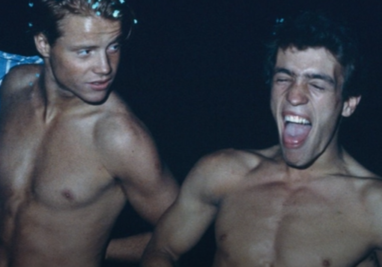 photo of two young topless men laughing in the dark