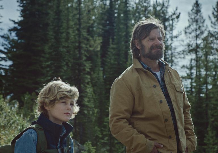 a father and child stand in nature with trees and grass behind them