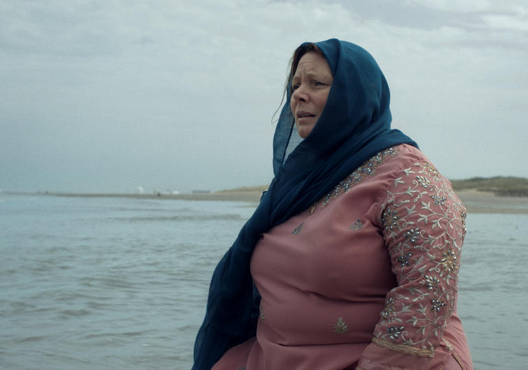 a woman wearing a hijab stands on the cliffs looking out to sea