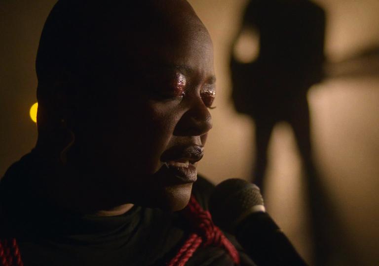 CLOSE UP PHOTO OF ESKA PERFORMING WITH GUITARIST IN BACKGROUND