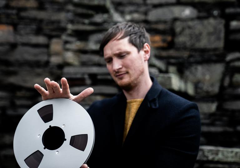 Erland Cooper, holding a film reel, wearing a suit 