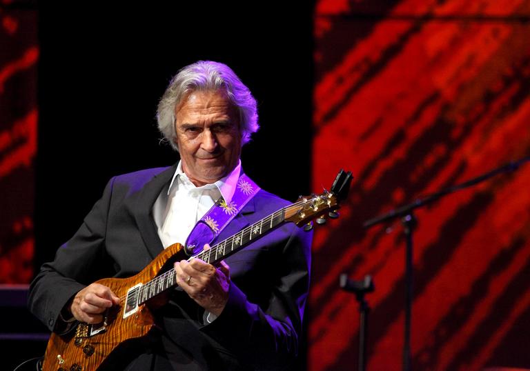 John McLaughlin playing guitar, wearing a suit