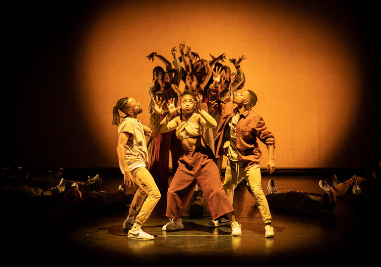 A group of people stand together with arms in the air and an orange light is shinning on them