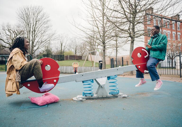 A man and woman sit on a seesaw 