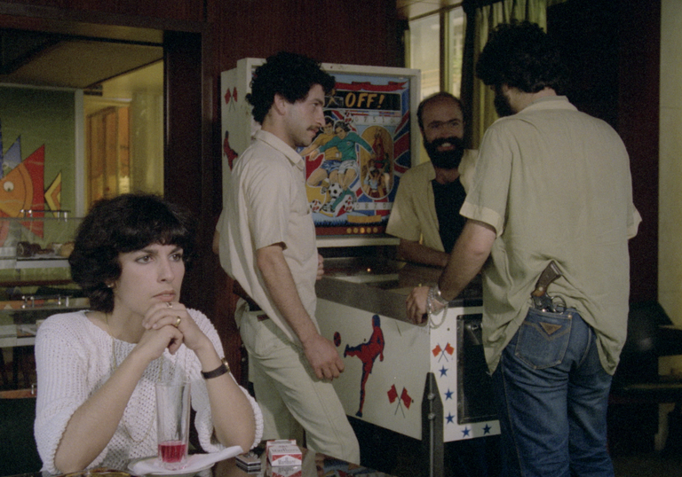 A group of people stand in a kitchen in a still from the film.