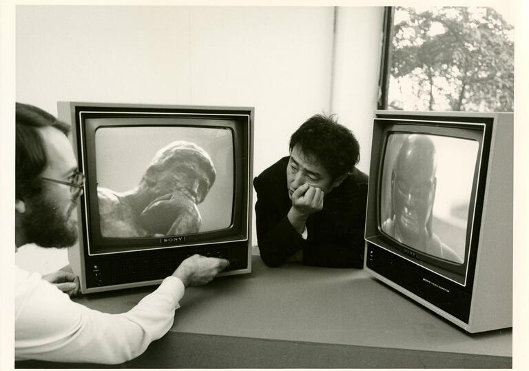 Paik looks at two TV screens in a still from Nam June Paik