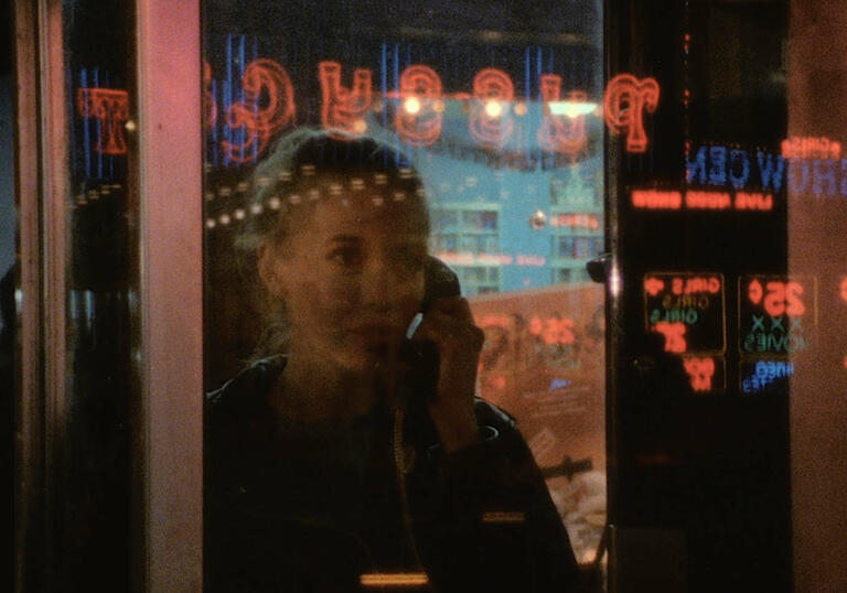 A woman looks longingly out of a cinema booth at the neon lights of the surrounding street