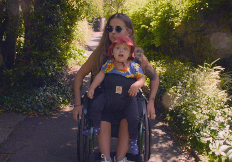 A mother in a wheelchair carries her young child through a flower lined path. 