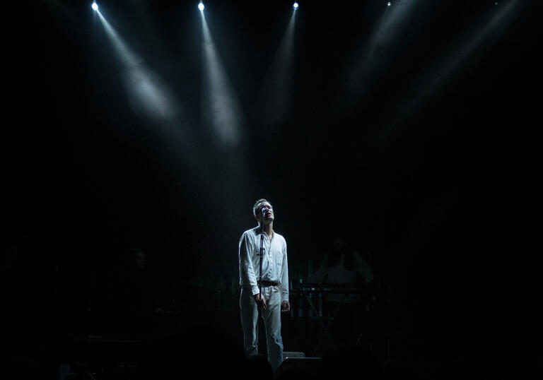 Efterklang stands on a dark stage, light with a spotlight