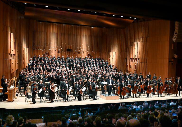 The Westminster School Symphony Orchestra and Choir, musicians from the Westminster Choral Society, Pimlico Musical Foundation and Tri-borough Music Hub standing on stage in the Barbican Hall