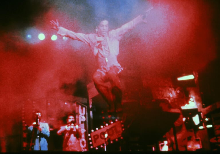 Prince jumps on a stage filled with a red mist. 