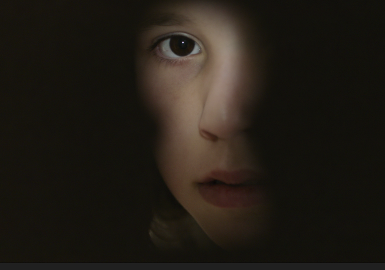 A young girl looks through a key hole. 