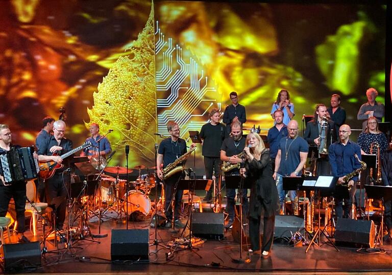 Maria Schneider and Oslo Jazz Ensemble perform on stage, surrounded by orange and yellow lights