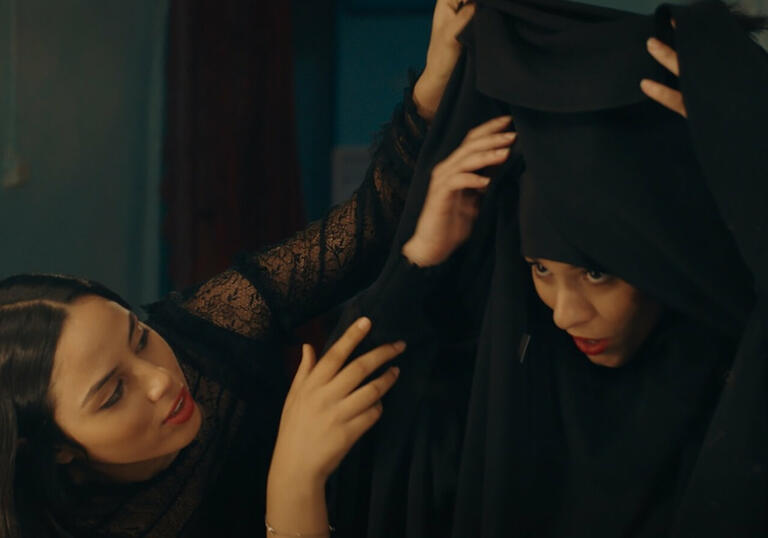 Two girls help their sister put on a head scarf.