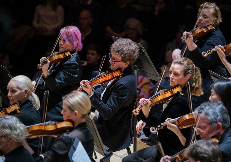 London SymphonyOrchestra string section performing on the Barbican Hall stage.