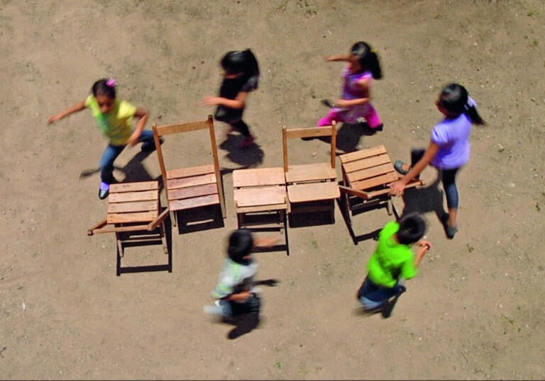 6 children running around 4 chairs, playing musical chairs