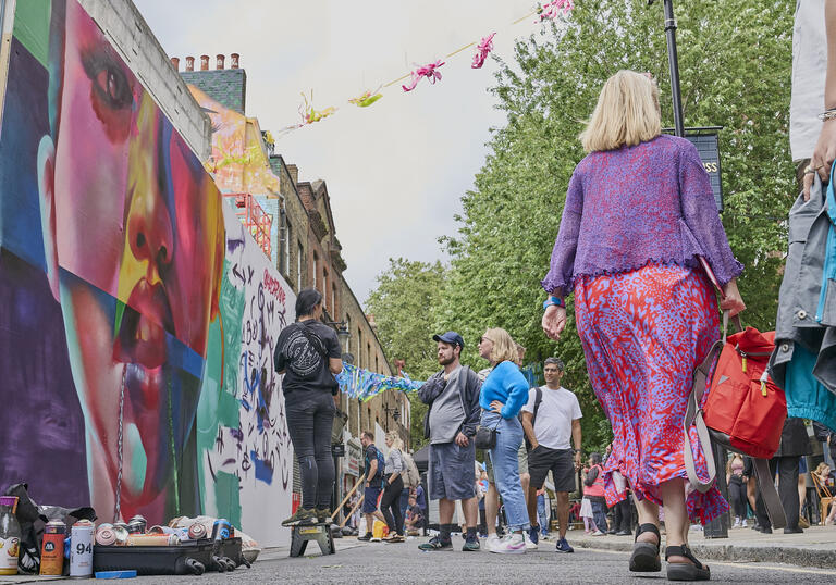 Graffiti on walls, people walking around and banners in sky at whitecross street part