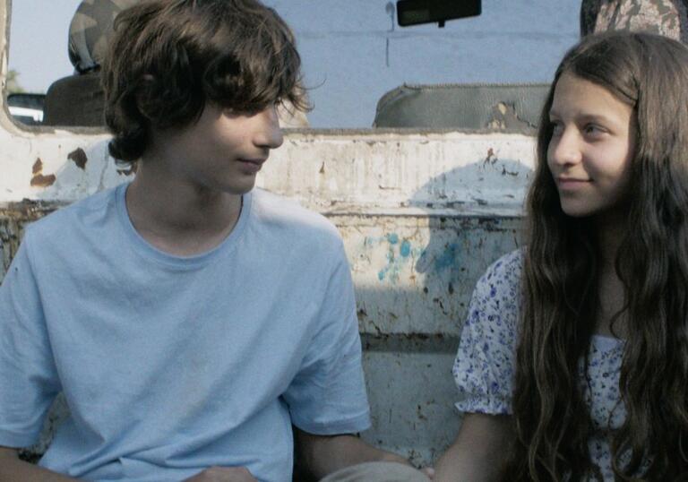 A boy and a girl smile at each other, sitting in the back of a pick up truck.