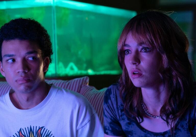 Two young teenagers sit in a dark room facing a TV.