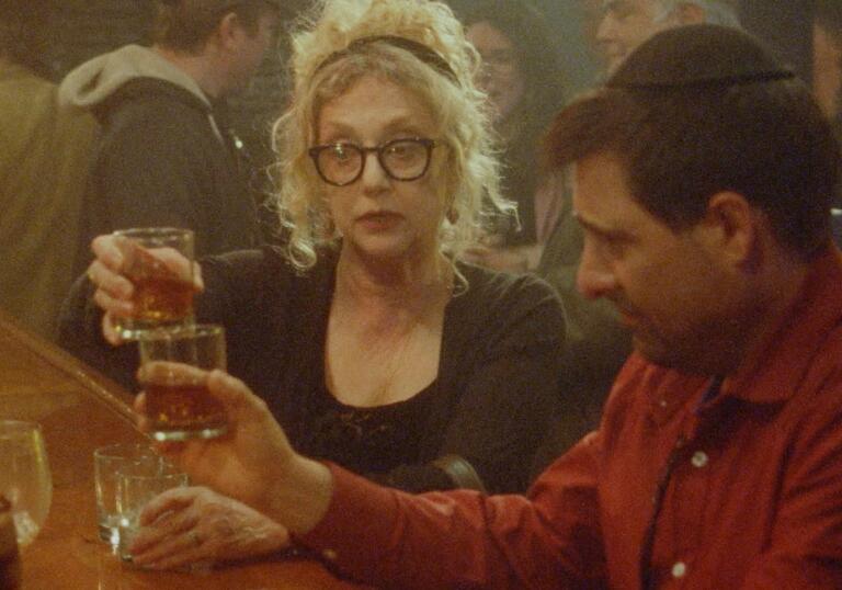 A man and a woman sit in a bar, and cheers each other. 