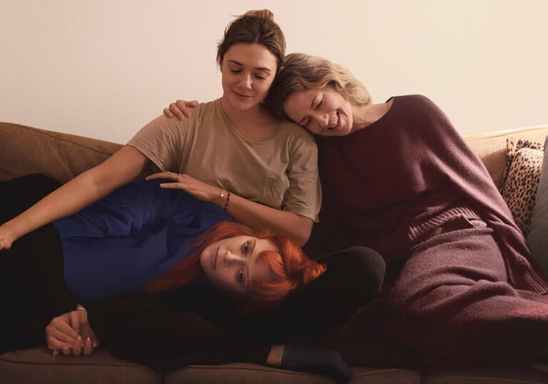 Three sisters sit on a sofa hugging each other. 