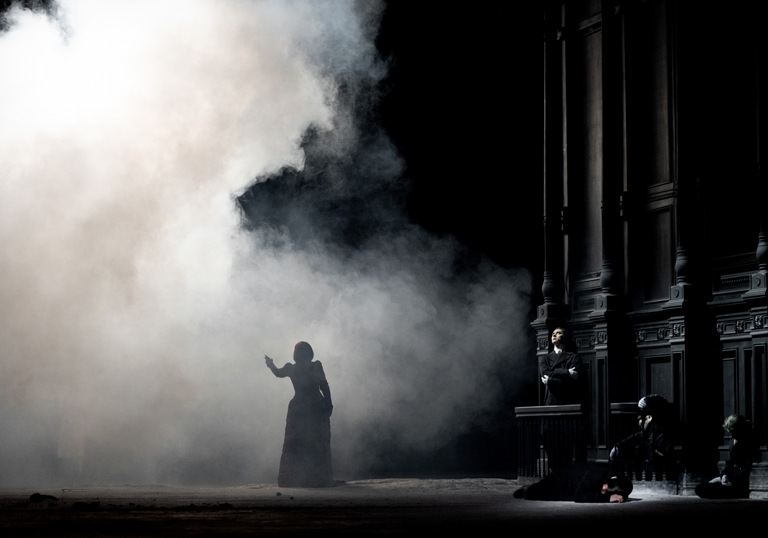 A woman stands in smoke on a dark stage.