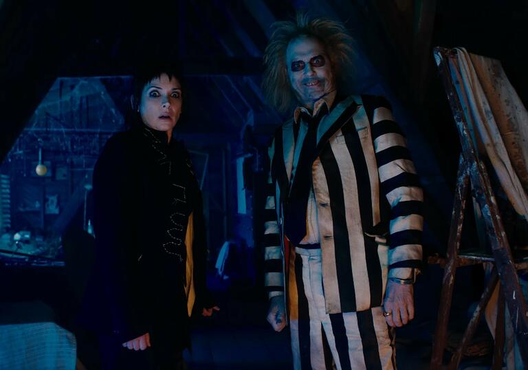 Lydia Deetz and Beetlejuice stand in a dark attic