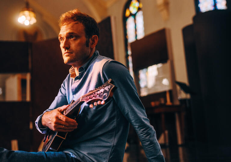 Chris Thile sitting in a room holding a mandolin