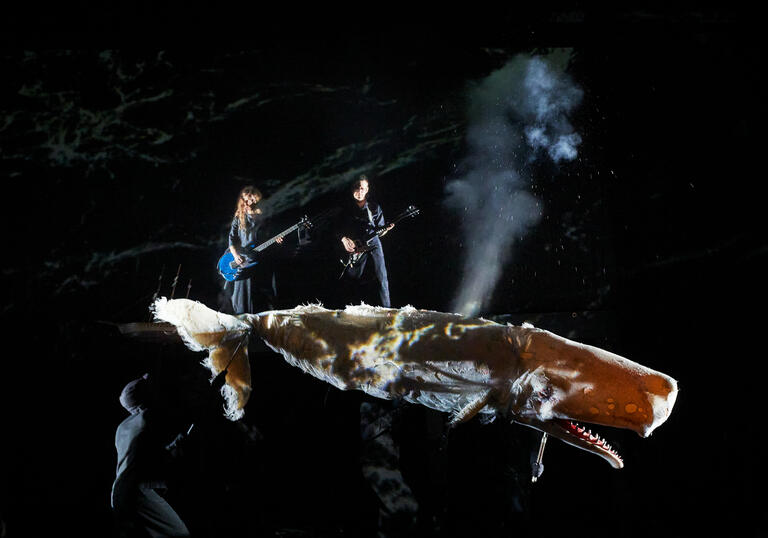 2 people playing electric guitars standing on top of a whale