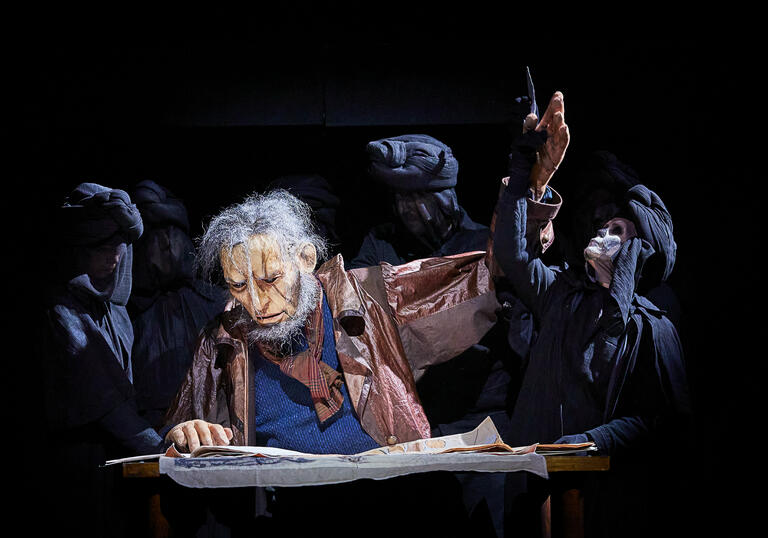 puppet grey-haired man reading, skeleton puppet in black cloak pulling the man's arm back