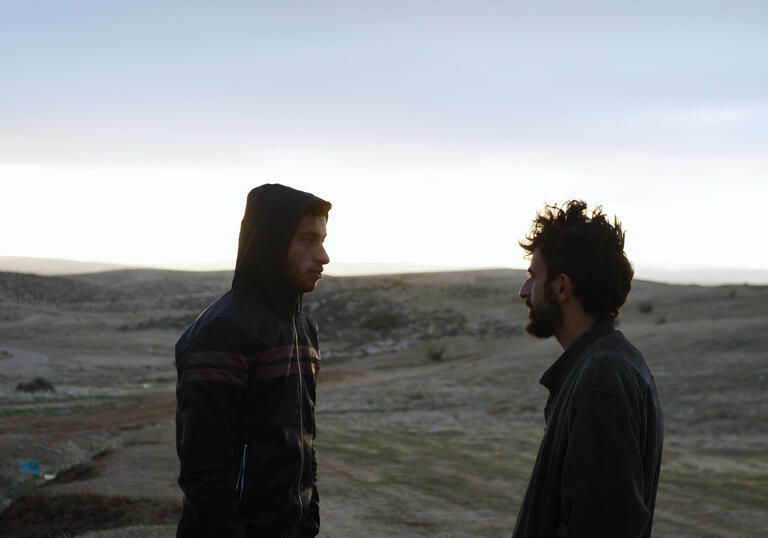 Two men stand facing each other in the desert 