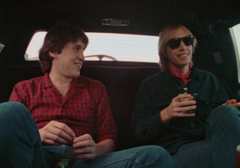 Two men sit in the back of a cab, chatting.