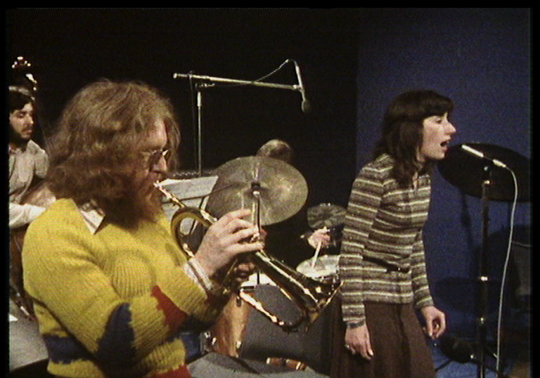 A jazz band in the 1970s plays in studio, a woman sings, a man plays the trumpet, and another plays the drums.