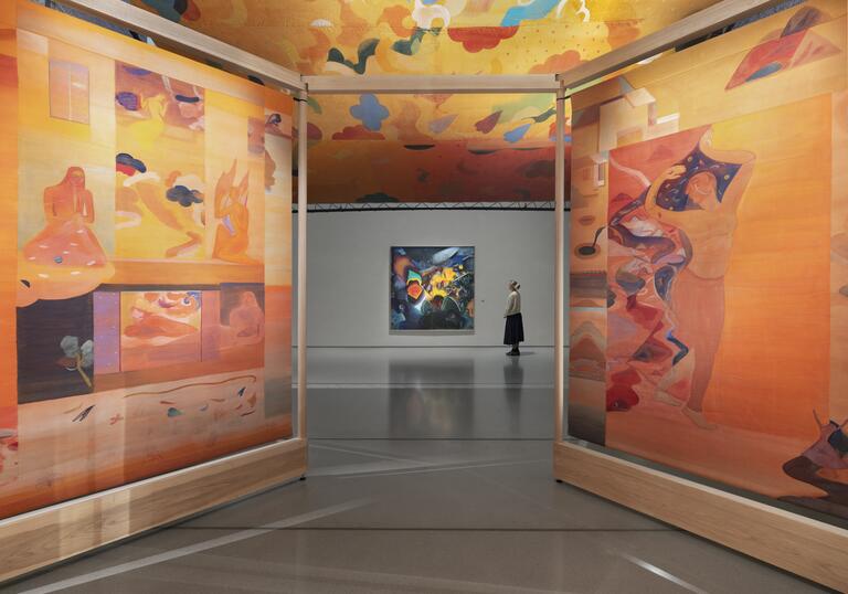 woman stands in front of a painting, taken from inside a colourful installation